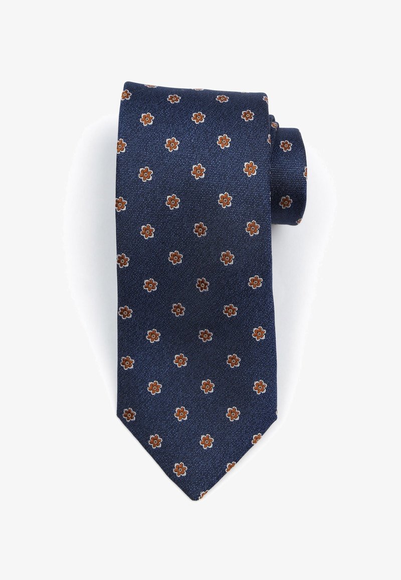 Donkerblauwe stropdas met een gestructureerde stof, voorzien van een klein bloemmotief in bruin en crème. Gevormd met een puntige tip en netjes opgerold.