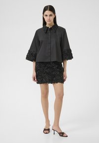 Blusa corta nera con dettagli floreali testurizzati sulle maniche, abbinata a una gonna nera con design floreali tridimensionali.