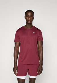 Bordeaux sportshirt met ronde hals en korte mouwen, voorzien van een klein wit logo op de borst, gecombineerd met bijpassende shorts.