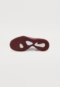Semelle de chaussure de sport rouge et blanche avec un motif de résistance texturé, deux découpes ovales et un logo Nike prononcé près du talon.