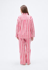 Σετ πιτζάμες με ριγέ κάθετες ρίγες σε ροζ και άσπρο, κατασκευασμένο από ελαφρύ ύφασμα, με άνετη εφαρμογή και μακριά μανίκια.
