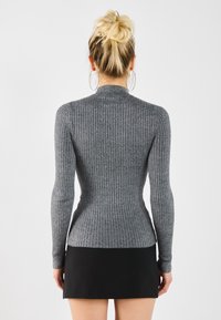 Fitted long-sleeve sweater in dark gray ribbed knit, back view. High neckline, slim silhouette, paired with a black mini skirt.