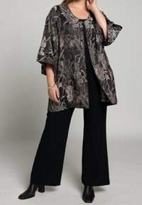 Zwarte kimono met bloemenpatroon en driekwart mouwen, open voorkant, gecombineerd met een zwart topje en wijde pijpen broek, aangevuld met enkellaarsjes.