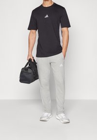 Svart t-shirt med vita sidstreck, grå sweatpants med vit Adidas-logga och en svart duffelväska. Avslappnad atletisk klädsel med matchande detaljer.