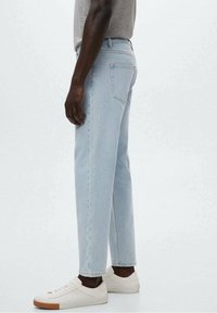 Jeans de mezclilla azul claro con corte recto, cinco bolsillos y una cinturilla clásica. Combinados con zapatillas blancas con suela marrón.