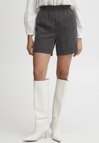 Gray cotton shorts with an elastic waistband, tailored fit, and folded hem, paired with high, white, ribbed leather boots.