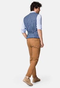 Sprawdzona niebieska kamizelka na jasnoniebieskiej koszuli w wzory, w połączeniu z dopasowanymi, beżowymi spodniami i beżowymi trampkami, tworząc warstwowy wygląd.