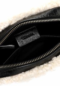 Interno di una borsa in pelle nera con una morbida fodera bianca e testurizzata. Presenta una chiusura con zip e un piccolo etichetta interna, circondata da un tessuto scuro.
