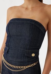 Strapless top van donkerdenim met een visgraatpatroon, gouden knoopaccenten en een decoratieve gouden kettingriem. Glad materiaal, getailleerde pasvorm.