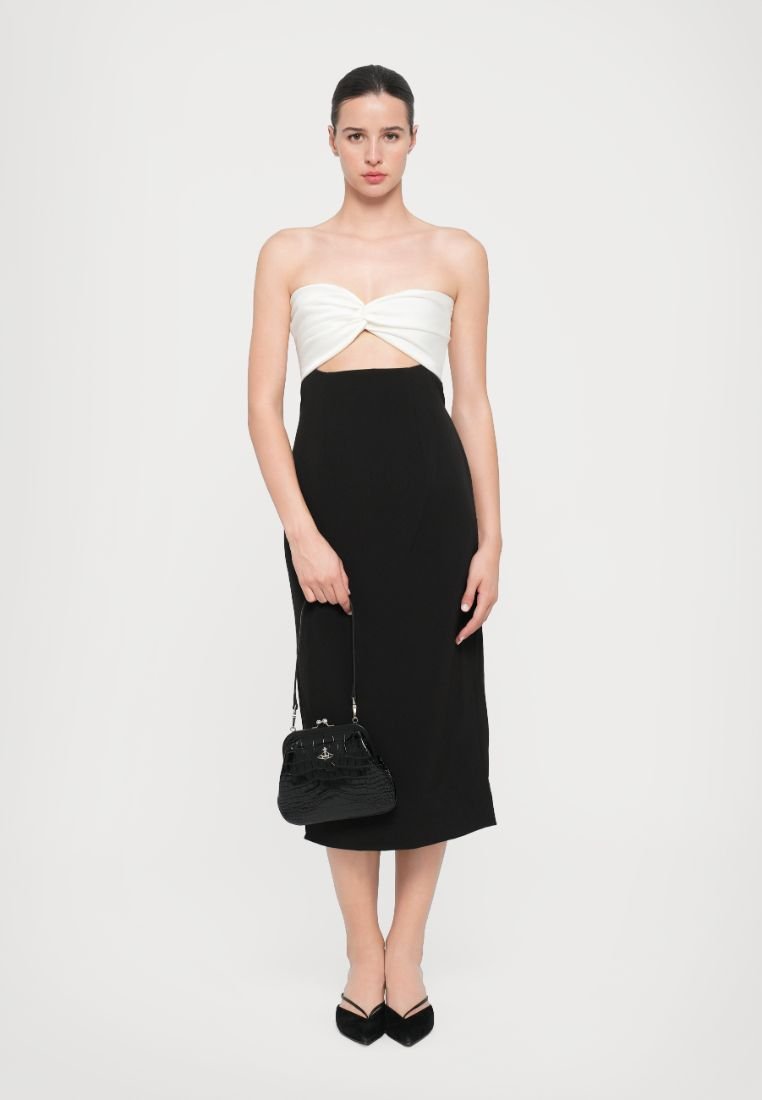 Robe noire midi avec un bodice sans bretelles blanc tordu, tissu texturé, assortie à un petit sac à main noir et des chaussures noires à talons pointus.