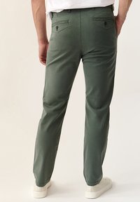Pantalones de algodón verdes con un corte recto, dos bolsillos traseros y una textura suave. Completados con zapatillas blancas.