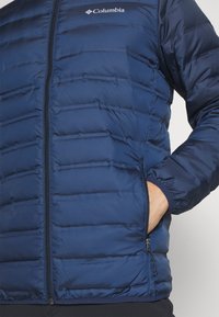 Giacca puffer navy con zip frontale, cuciture orizzontali, polsini elasticizzati e logo Columbia sul petto. Materiale resistente e isolato.
