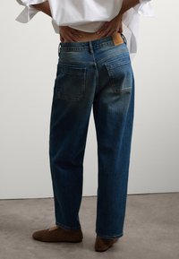 Jeans de mezclilla azul con un corte relajado, que cuentan con una etiqueta de cuero en la parte trasera de la cintura y dos bolsillos traseros. Parte delantera plana y piernas rectas.