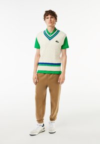 Cream cable-knit vest over a green polo, featuring blue and green horizontal stripes. Brown sweatpants and white sneakers complete the outfit.