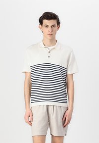 Polo shirt à manches courtes en crème avec des rayures horizontales bleu marine, doté d'un col et d'une patte de boutonnage à trois boutons, associé à un short gris clair.