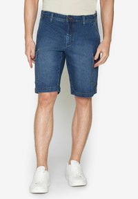 Shorts in denim blu scuro con taglio dritto, dotati di tasche laterali e vita regolare. Abbinati a sneakers bianche.