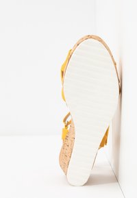 Gul kilklack sandal med en korktexturerad klack, vit gummisula och justerbar rem. Slät läderöverdel med minimala hårdvaruaccentueringar.