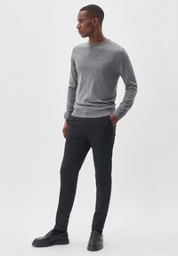 Pelēks garām piedurknēm svīteris apvienots ar melnām šaurām biksēm un melnām slip-on kurpēm, uz balta fona.