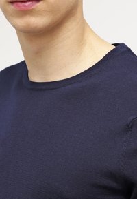 Granatowy sweter z okrągłym dekoltem, wykonany z dzianiny o gładkiej fakturze, z krótkimi rękawami i prążkowanym wykończeniem przy kołnierzu oraz krawędziach rękawów.