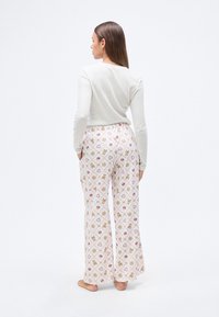 Ανοιχτόχρωμο πουκάμισο μακρυμάνικο συνδυασμένο με φαρδιά παντελόνια με σχέδια από κουλουράκια gingerbread, καρδιές και νιφάδες χιονιού σε ροζ και χρυσαφί αποχρώσεις.