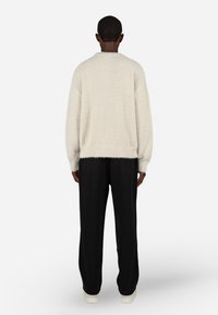 Svetlo siva, puhasta majica s udobnim krojem, rebrastim izrezom i dugimi rokavi, v kombinaciji s črnimi, ohlapnimi hlačami.