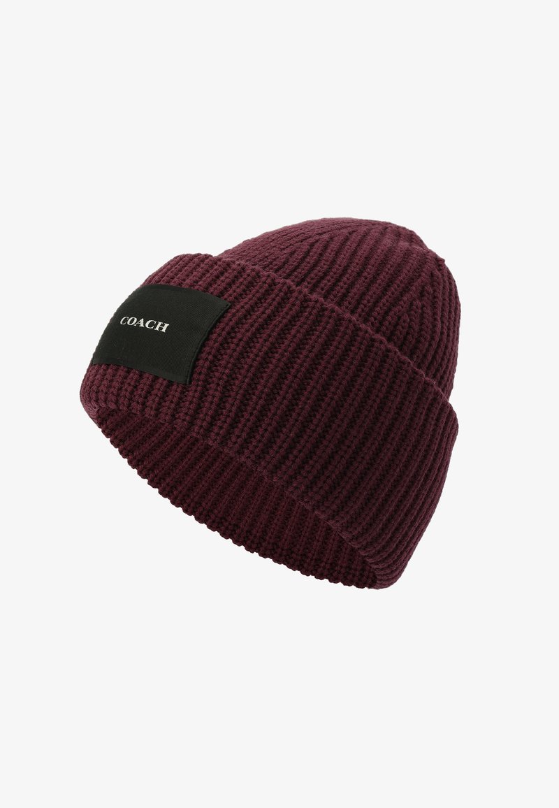 Gorra de punto color burdeos con una textura acanalada. Presenta una etiqueta rectangular negra con texto en relieve blanco en el lateral. Material suave y elástico.