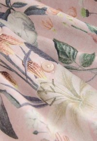 Látka s květinovým vzorem v odstínech růžové, s krémovými knoflíky. Design zahrnuje různé květiny a listy s jemným, texturovaným vzhledem.