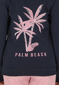 Felpa navy con grafica di palme rosa e testo "PALM BEACH". Tessuto morbido con vestibilità rilassata e polsini a costine.