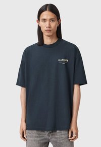 Σκούρο μπλε σκούρο μπλουζάκι oversized από βαμβάκι, με μικρό κίτρινο λογότυπο στο αριστερό στήθος και κοντά μανίκια, με στρογγυλή λαιμόκοψη.