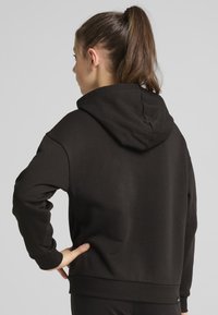 Svart bomullshuvtröja med en avslappnad passform, som har en huva och ribbade muddar. Minimalistisk design, med en liten logotyp som accent vid fållen.