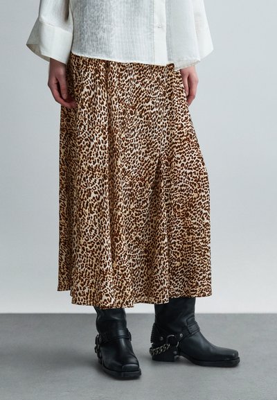 Falda midi con estampado de leopardo en tonos beige y marrón, confeccionada en tela ligera. Se lleva con botas negras de cuero hasta la mitad de la pantorrilla, con detalles de hebillas.