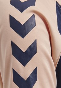 Ljust rosa tyg med en vertikal rad av fyra stora mörkblå chevronformer, närbild som visar textur och sömnad.