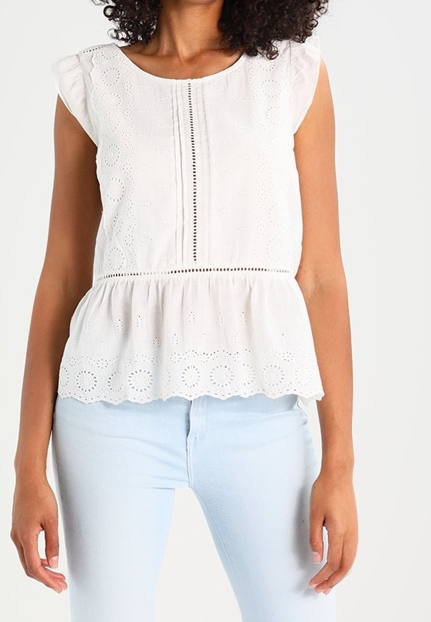 Top en coton blanc à peplum avec des manches courtes et volantes, un design de broderie délicate, et une patte décorative avec des boutons le long du centre.