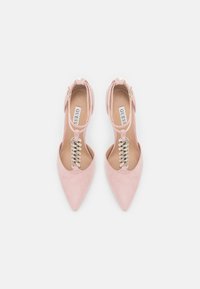 Růžové semišové lodičky s úzkou špičkou, ankletovým páskem, kovovým šněrováním a hladkým povrchem. Značka viditelná na vnitřní straně stélky.