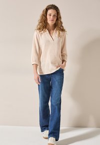 Blouse texturée rose clair avec un col en V et des manches trois-quarts, associée à un jean large bleu et des baskets beiges.