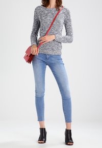 Harmaa- ja valkoinen tekstuurineulepaita, siniset kapealahkeiset farkut, mustat avokkaat ja punainen olan yli kantava laukku. Lookissa on rento tyyli.