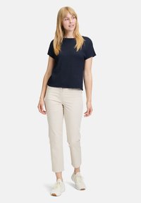 Top corto blu strutturato abbinato a pantaloni beige aderenti e sneakers bianche. Il top presenta un colletto a girocollo e una vestibilità ampia.