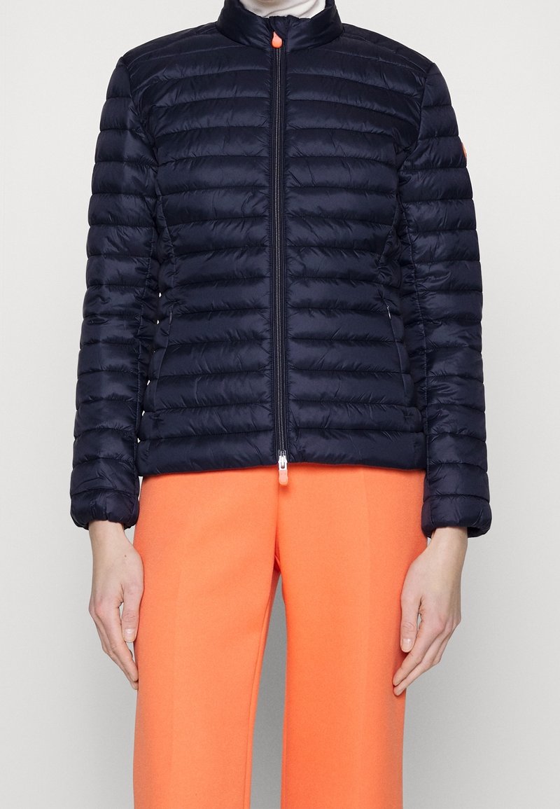 Granatowa kurtka puchowa z wysokim kołnierzem, zamkiem błyskawicznym z przodu i pikowanym wzorem. Materiał jest gładki i błyszczący, z pomarańczowym akcentem na zamku.