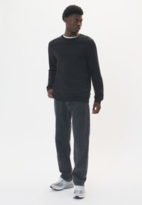 Čierna mikina s okrúhlym výstrihom v kombinácii s tmavošedými rovnými džínami a šedými teniskami s bielymi akcentmi. Celková hladká textúra.