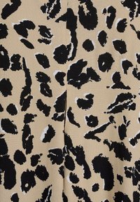 Das Leopardenmuster-Gewebe hat einen beigen Hintergrund mit schwarzen und weißen Flecken. Die Textur wirkt glatt mit einem leichten Glanz.