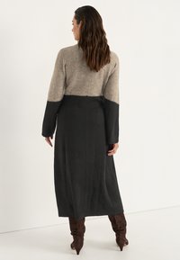 Lång klänning med en beige överdel och svart nederdel, med långa ärmar och en texturerad väv. Bruna knähöga stövlar fulländar looken.