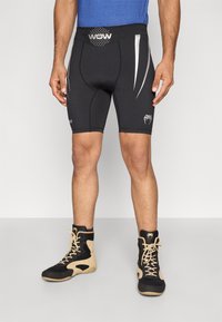 Calções de compressão pretos com detalhes prateados, com ajuste justo e cintura elástica. Usados com sapatilhas desportivas de cano alto em preto e castanho.