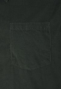 Tela de pana de color verde oscuro con un único bolsillo trasero en ángulo que presenta detalles de costura sutiles y un patrón acanalado texturizado.