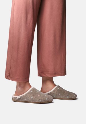 Pieds portant des chaussons marron décorés de petites étoiles pastel, assortis à un pantalon ample et court de couleur rouille sur fond blanc.
