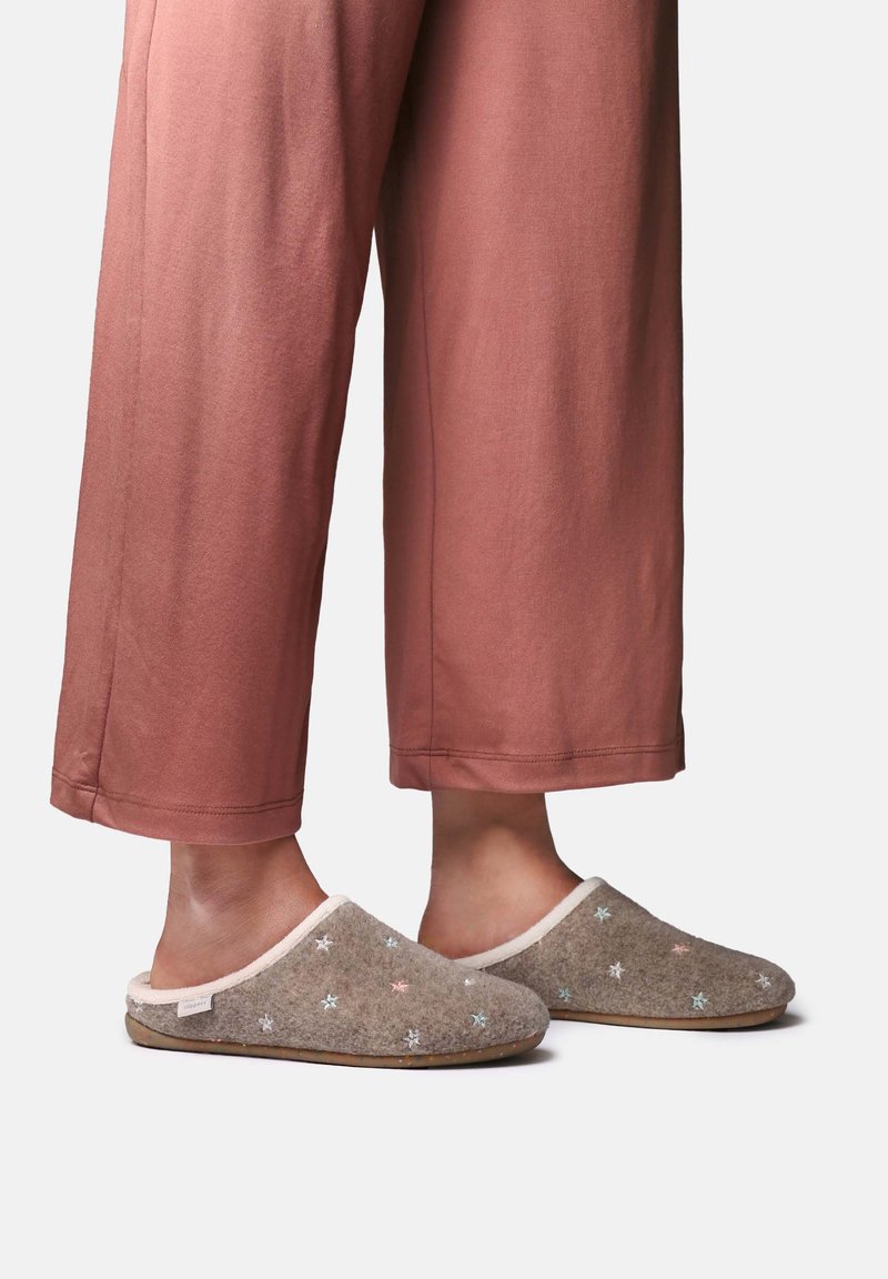 Pieds portant des chaussons marron décorés de petites étoiles pastel, assortis à un pantalon ample et court de couleur rouille sur fond blanc.