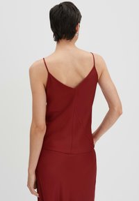 Bordeaux satijnen camisole met dunne bandjes, met een V-achterkant en naadloze stiksels, die een gladde en vloeiende textuur benadrukt.