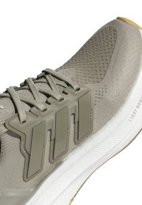 Beige sportsko med mesh-overdel, struktureret overflade og grå detaljer. Har fremtrædende gummioverflader og en hvid, struktureret sål.