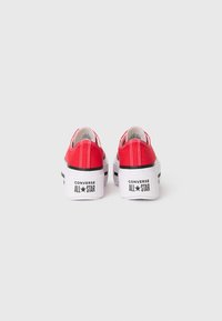 Crvene platnene tenisice s niskim dizajnom, bijelim platformama i crnim detaljima, sa "Converse All Star" logotipom na peti.