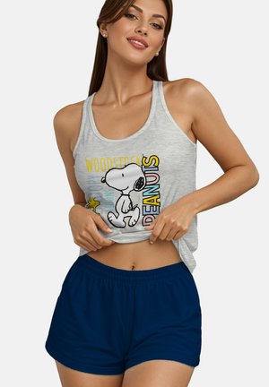 Frau trägt graues Tanktop mit Snoopy- und Woodstock-Motiven und marineblaue Shorts und hält den Saum ihres Shirts.
