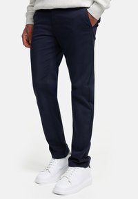 Chinos azul marino de tejido suave con un corte entallado; cuentan con bolsillos y se combinan con zapatillas blancas para un look casual.